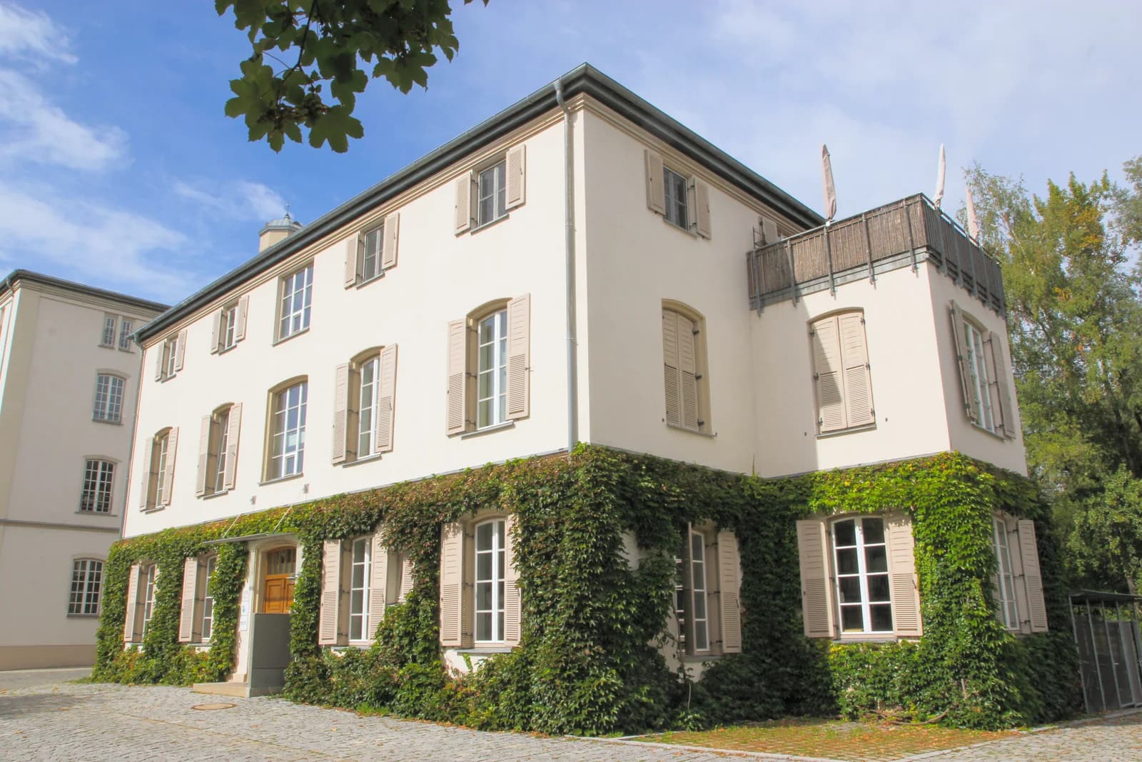 Das Bürogebäude in der Kunstmühlstraße 17 in Rosenheim, ein helles Haus mit Fensterläden und begrüntem Erdgeschoss